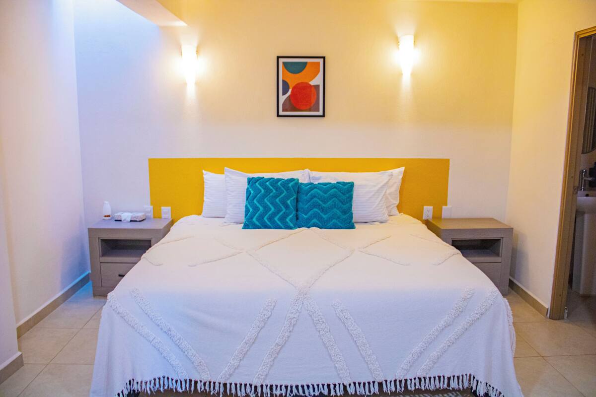 Een hotelkamer met een bed, twee nachtkastjes, een wandlamp en een lijst met een afbeelding.