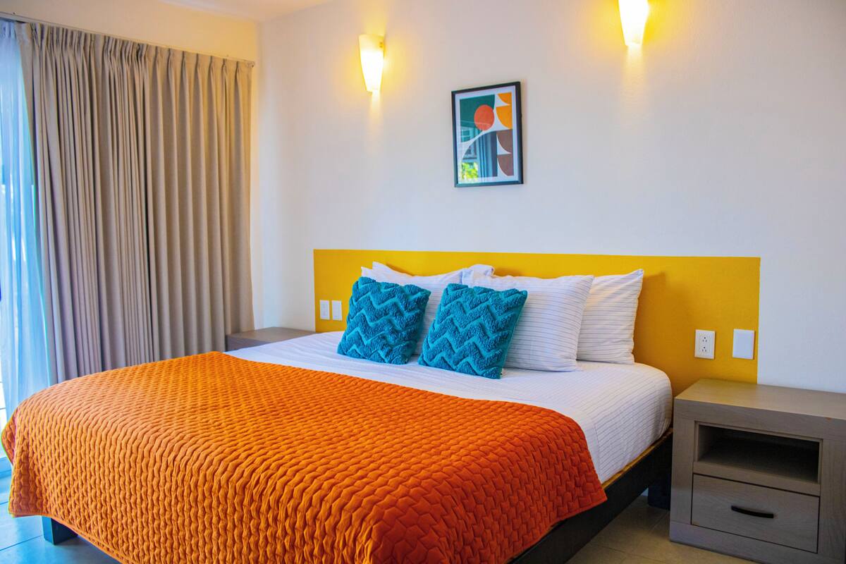 Een hotelkamer met een bed, gordijnen, een nachtkastje en een wandlamp.