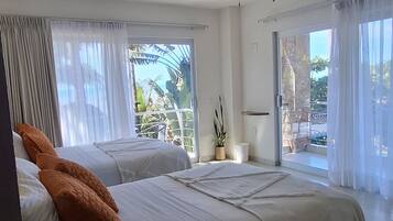 Ein Hotelzimmer mit zwei Betten, einem Deckenventilator, großen Fenstern mit Vorhängen und Blick ins Freie.