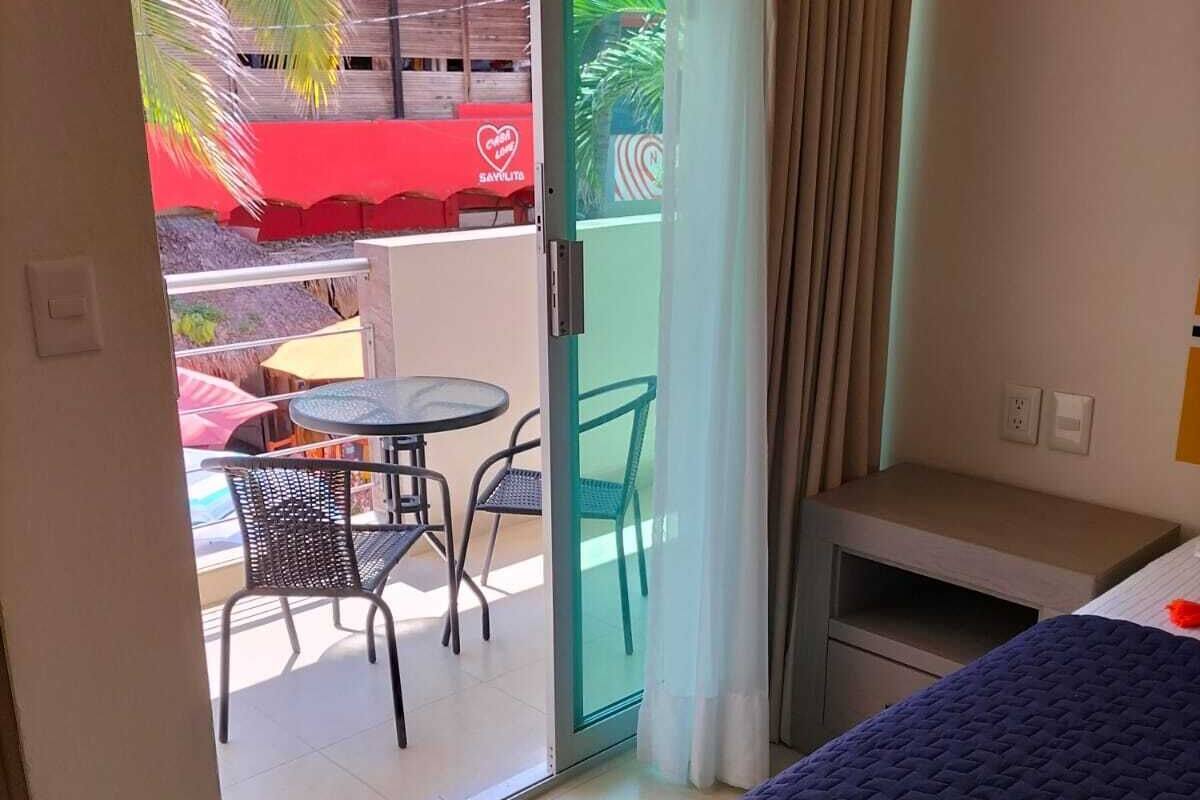 Hotelkamer met een bed, een klein tafeltje, een stoel en een glazen schuifdeur naar een buitenruimte met een tafel en stoelen.