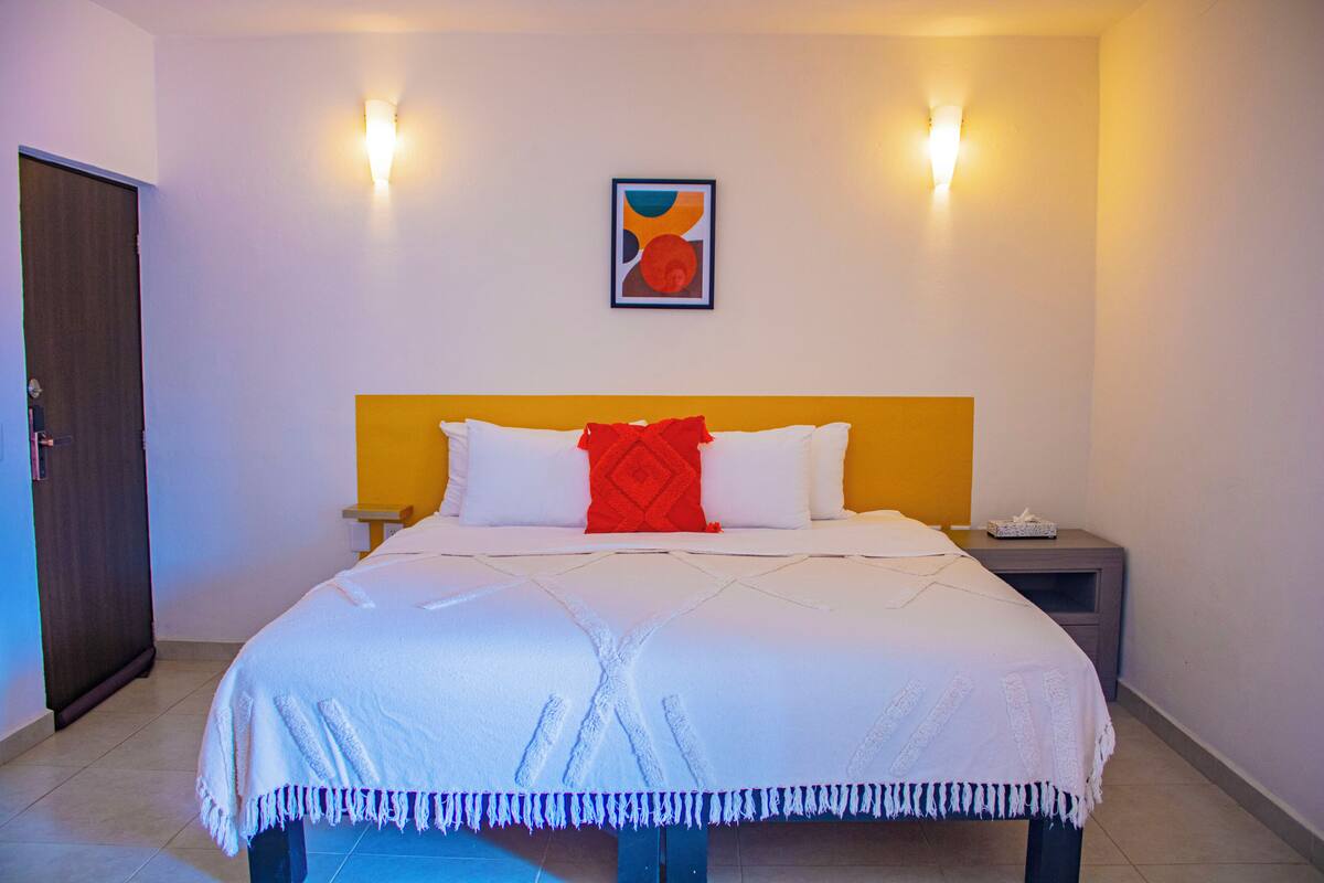 Een hotelkamer met een bed, nachtkastje, wandkunst en een deur.