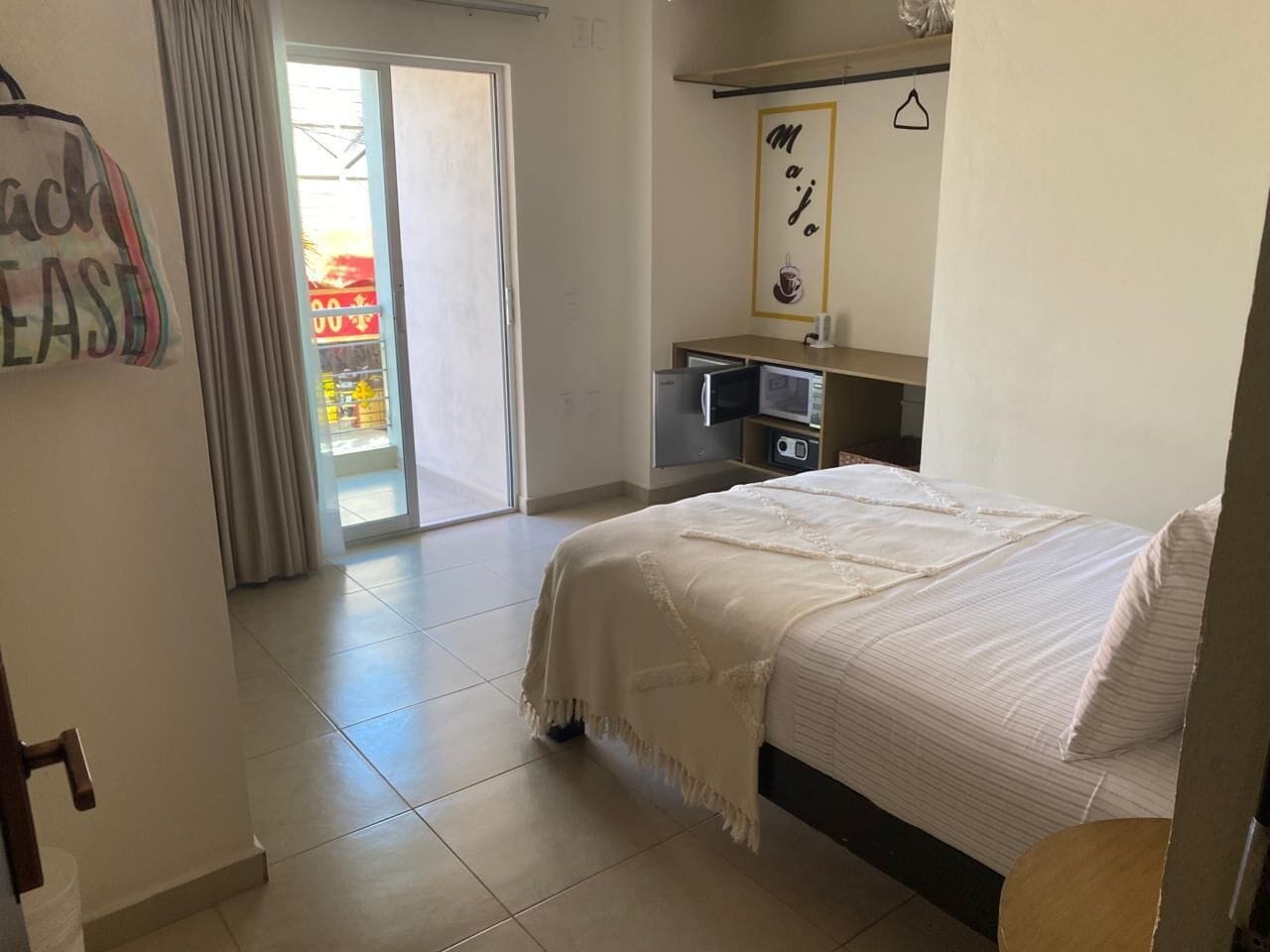 A bedroom with a bed, a desk with a computer, a mirror, and a door leading to a balcony.