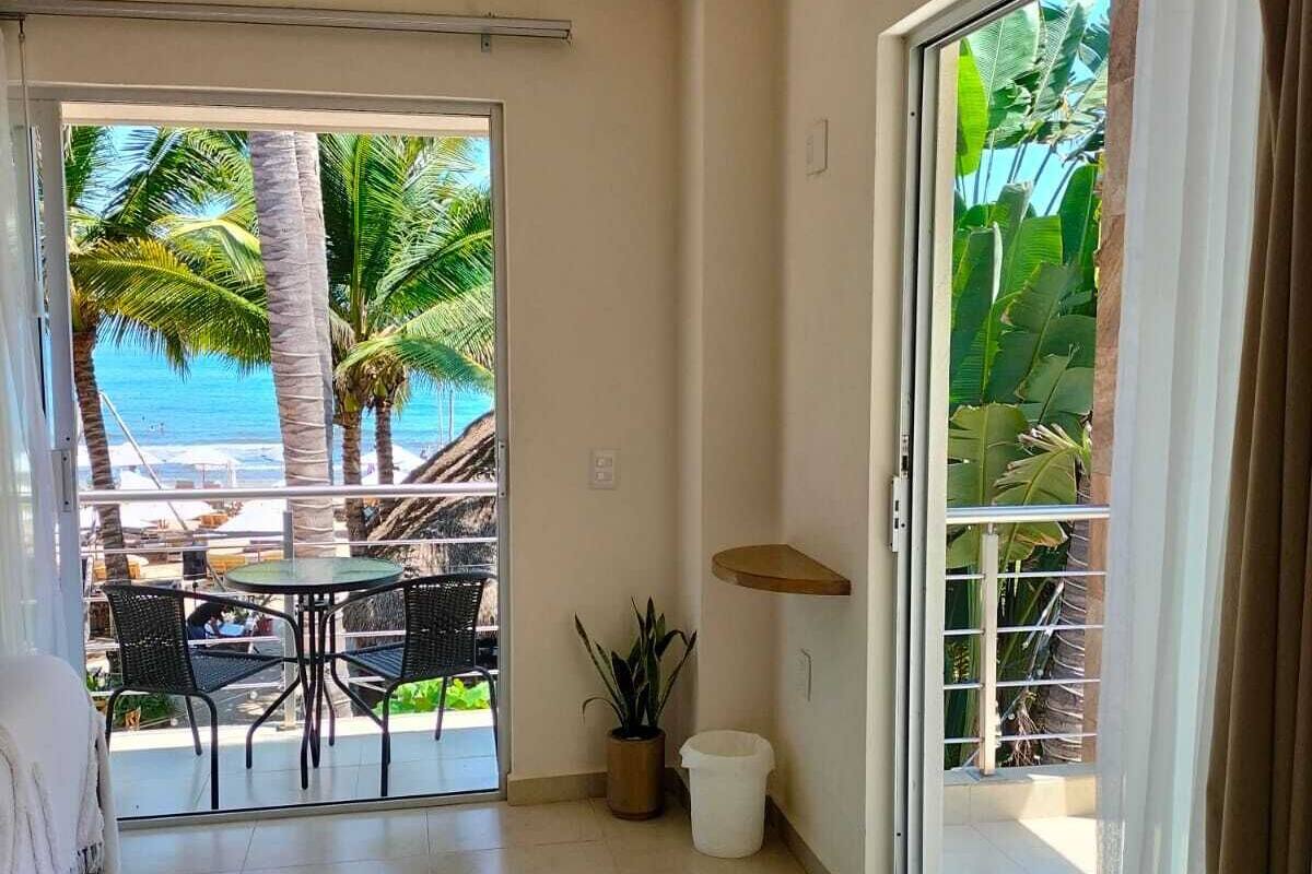 Een kamer met een schuifdeur die uitkomt op een balkon met uitzicht op het strand en palmbomen.