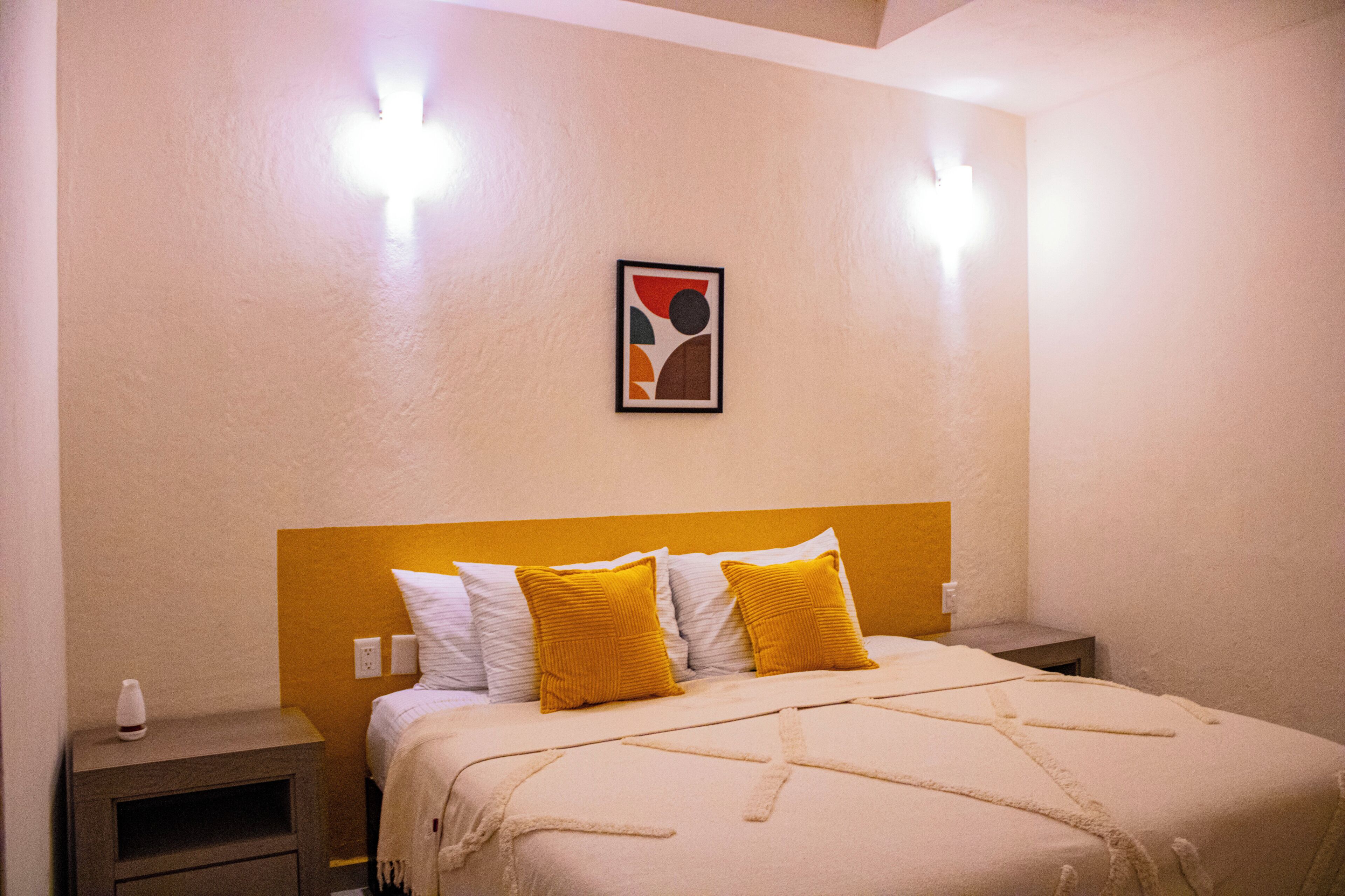 Une chambre à coucher avec un lit, deux tables de chevet, une lampe fixée au mur et un tableau encadré.
