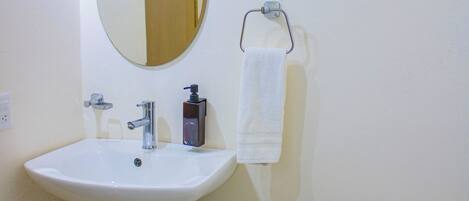 A bathroom with a sink, mirror, toilet, and trash bin.