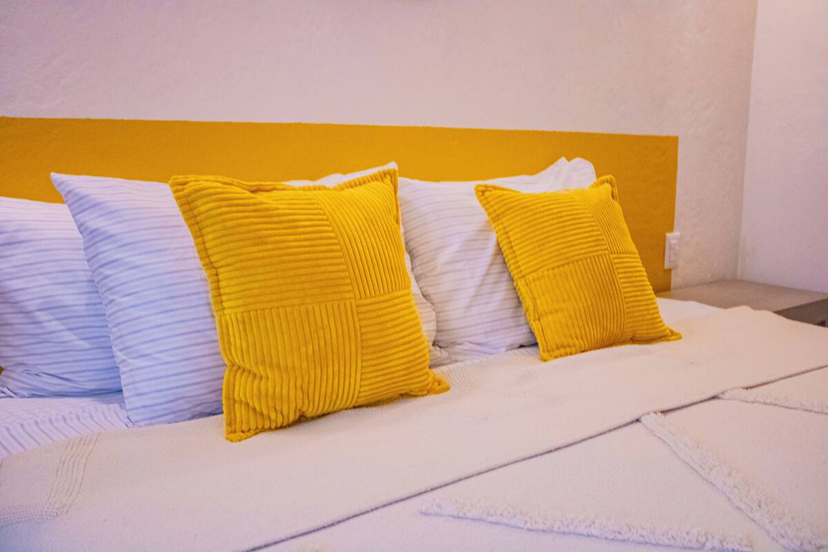 Een bed met witte en gele kussens, een wit hoofdbord en een witte deken.