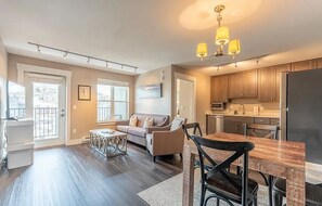 A modern apartment with a living room, dining area, kitchen, and large windows. - Cozy Mountain Escape | Near Lifts + Trails (Mt. Crested Butte)
