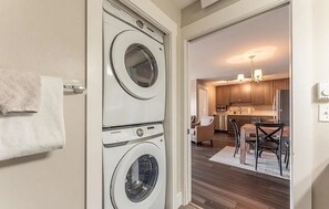 A laundry area with two front-loading washers, a kitchen with wooden cabinets, a dining area with a table and chairs, and a hallway leading to a living space. - Cozy Mountain Escape | Near Lifts + Trails (Mt. Crested Butte)