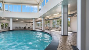 Una piscina interior con agua azul cristalina, rodeada de sillones de descanso y un suelo de baldosas de piedra.