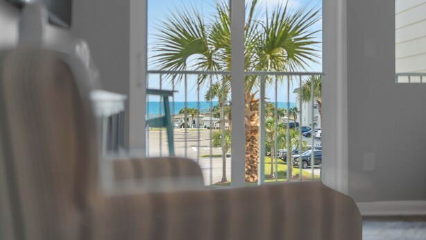 Vista desde una ventana con palmeras y un edificio al otro lado de la calle.
