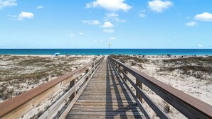 Un muelle de madera que conduce a una playa, con cielo despejado y horizonte lejano.