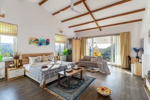 Un dormitorio amplio con una cama grande, un sofá, una silla colgante y vistas al exterior.