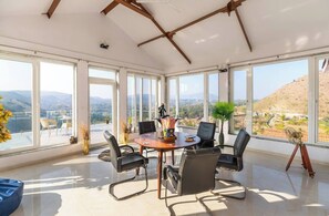 Una habitación amplia con una mesa grande, sillas y vistas a un paisaje montañoso a través de amplios ventanales.
