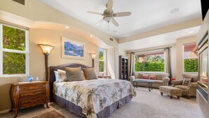 Une chambre à coucher comprenant un lit, un bureau, une chaise, un canapé, un ventilateur de plafond et de grandes fenêtres.