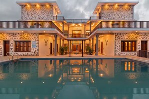 A two-story building with a swimming pool in front, stone walls, and balconies.