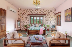 A room with a bed, two armchairs, a coffee table, a chandelier, and a large window with a view.