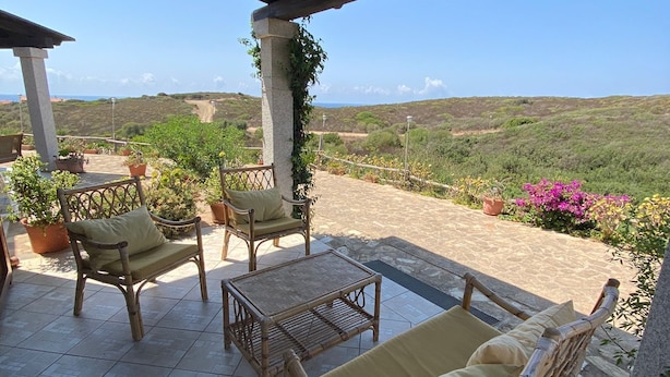 Un patio al aire libre con mobiliario de mimbre, suelo de piedra y vistas al campo.