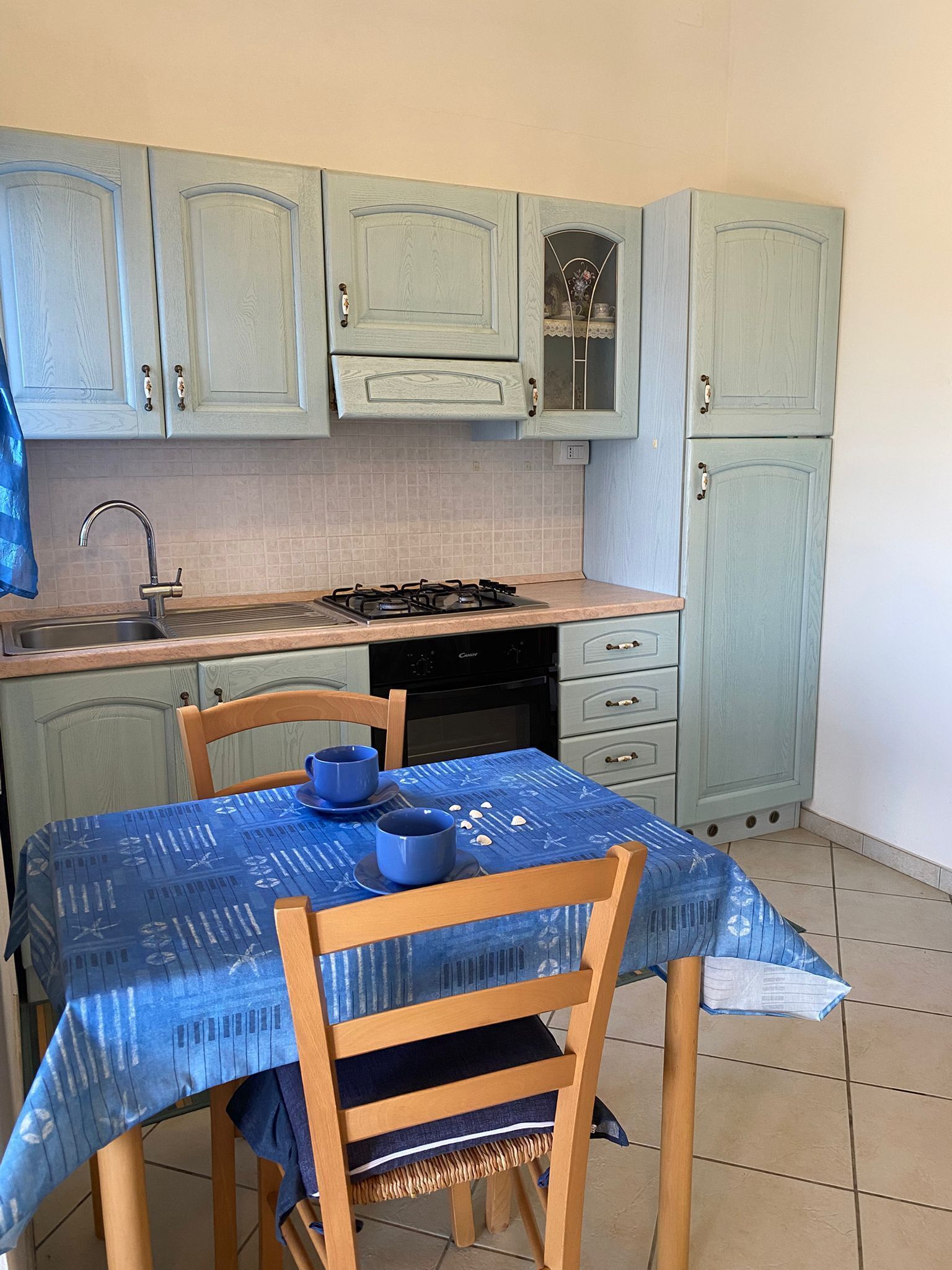 Uma cozinha com armários azul claro, fogão a gás, pia e mesa com toalha de mesa azul.