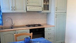 Una cocina con armarios azul claro, estufa a gas, un lavamanos y una mesa con mantel azul.