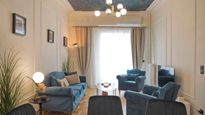 Un salon comprenant un canapé, des fauteuils, une table, une plante et un luminaire fixé au plafond.