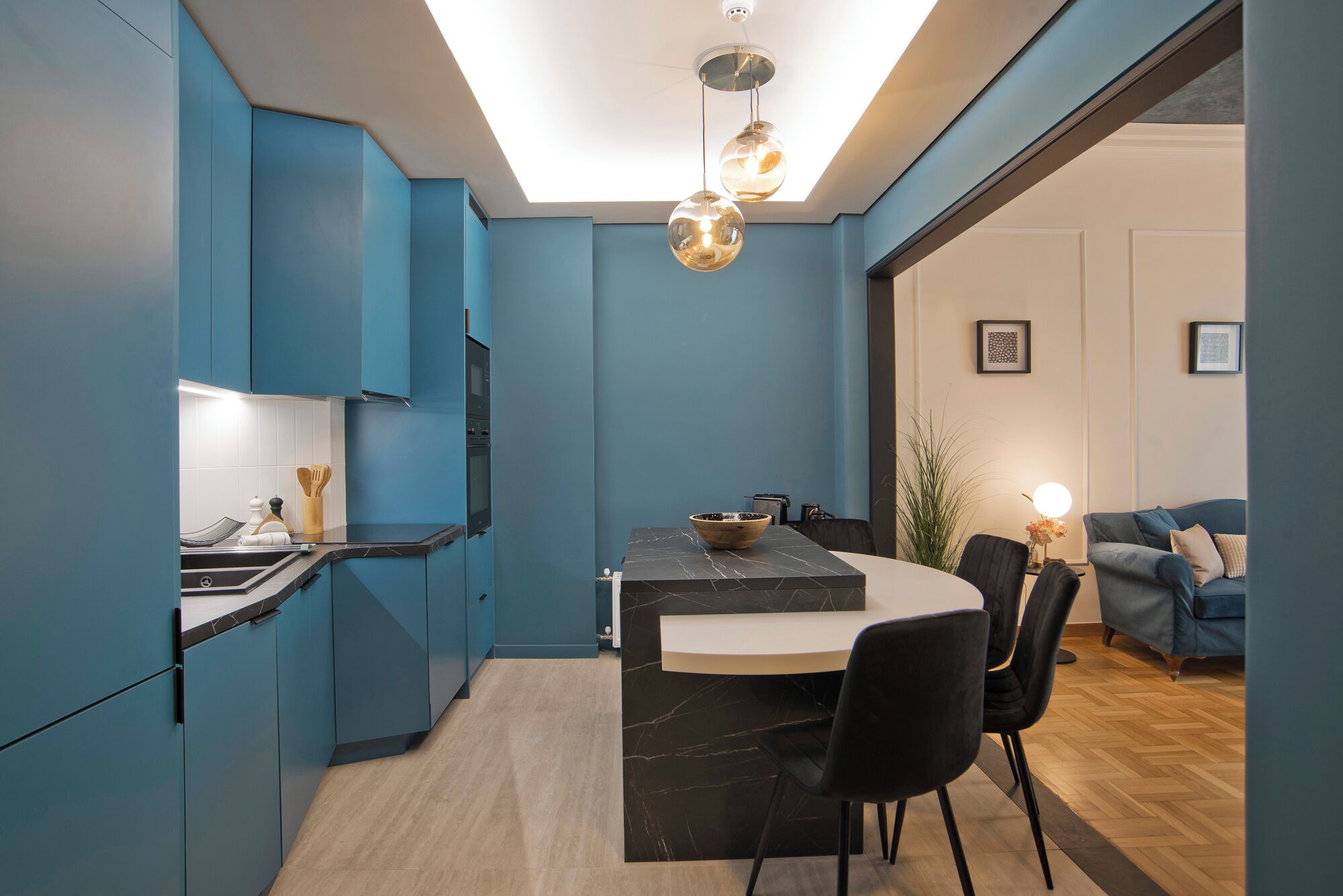 A modern kitchen with blue cabinets, a marble island, and a dining area with black chairs.