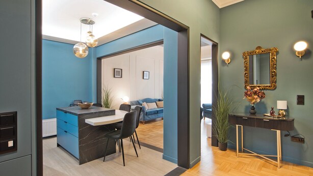 Un intérieur moderne comprenant une cuisine, un coin repas et un espace de vie, avec un mur bleu, un plancher en bois et une décoration contemporaine.