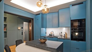 Une cuisine moderne avec des meubles de rangement bleus, un plan de travail en marbre et une table de salle à manger ronde, accompagnée de chaises.