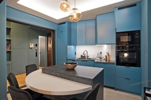 A modern kitchen with blue cabinetry, a marble countertop, and a round dining table with chairs. - Maison Kolonaki – Timeless Athenian Elegance (Athina)