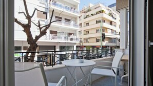 Un balcon avec une table et des chaises, un arbre et une vue sur des immeubles à plusieurs étages.
