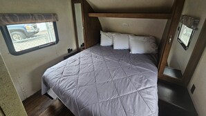 Ein kleines Schlafzimmer in einem Wohnmobil mit Bett, Fenster und Spiegel.