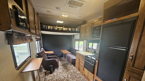 Eine kleine Küchenzeile für Wohnmobile mit Herd, Spüle und Kühlschrank, mit einem gemusterten Teppich und Holzschränken.