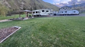 Ein Campingplatz mit Wohnmobilen, einer Laube und einem Haus in einer gebirgigen Gegend.