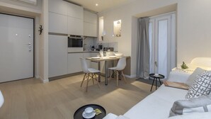 Een compacte leefruimte met een kitchenette, een eethoek en een zithoek met een bank en een klein tafeltje.