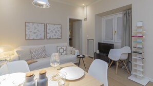 Een moderne woonkamer met een bank, een eettafel en stoelen. Er is een televisie, een open haard en een boekenkast.