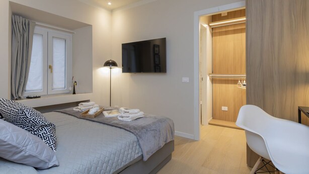 Een slaapkamer met een bed, een televisie, een bedlampje, een kledingkast en een stoel.