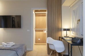 A hotel room with a bed, a desk with a chair, a television, and a wardrobe. - One-bedroom apartment on the first floor in the heart of Brera, Milan’s artistic and bohemian district. A strategic location just steps from the Pinacoteca di Brera, La Scala Theatre, and Castello Sforzesco.An elegant apartment offering all modern comf (Milan)