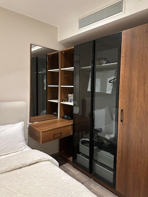 Une chambre à coucher comprenant un lit, une table de chevet en bois, un miroir, une armoire avec des portes en verre et une étagère intégrée.