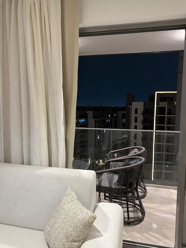 A balcony with a sofa and wicker chairs, overlooking a cityscape at night.