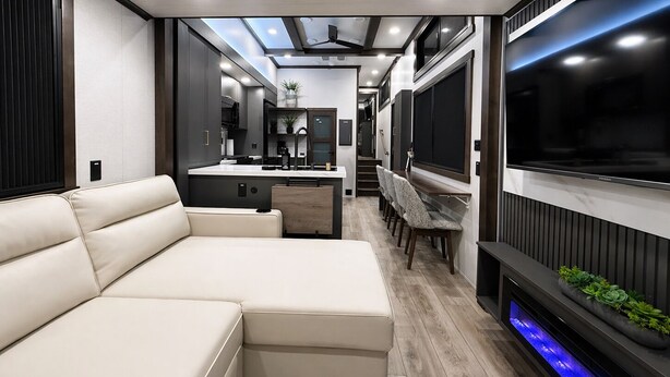 Un interno camper moderno con divano, angolo cottura, TV e una fontana illuminata di blu.