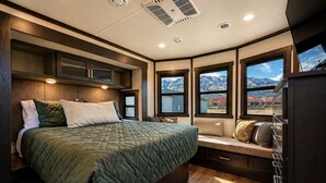 Una camera da letto con un letto grande, scaffali a muro, una panca contenitore e vista sulle montagne attraverso le finestre.