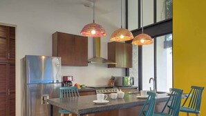 A modern kitchen with a stainless steel refrigerator, wooden cabinets, a central island with blue chairs, and pendant lights. - Casa Chopin Stylish Home in Santiago (Mérida)