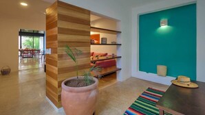 A modern interior with a wooden accent wall, a large terracotta pot with a plant, a colorful striped rug, and a teal accent wall with a light fixture. - Casa Chopin Stylish Home in Santiago (Mérida)