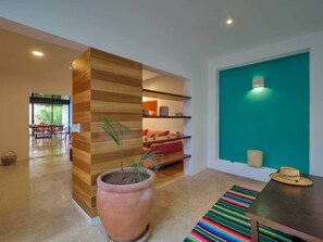 A modern interior with a wooden accent wall, a large terracotta pot with a plant, a colorful striped rug, and a teal accent wall with a light fixture. - Casa Chopin Stylish Home in Santiago (Mérida)