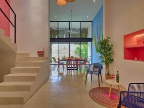 A modern interior with a staircase, a dining area with a table and chairs, a potted plant, and a small table with a wine bottle. - Casa Chopin Stylish Home in Santiago (Mérida)