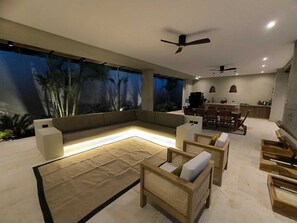 Un espacio de estar moderno con un ventanal grande, un sofá, una mesa de comedor y dos ventiladores de techo.