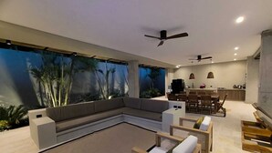 A modern living area with a sectional sofa, a dining table, and chairs, a kitchen in the background, and a large wall mural. - Large Farm via Villeta in Closed Condominium (Villeta)
