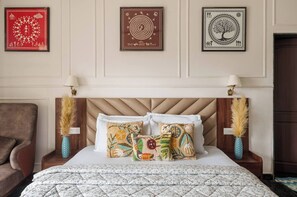 A hotel room with a bed, two nightstands, a chair, and three framed artworks on the wall.