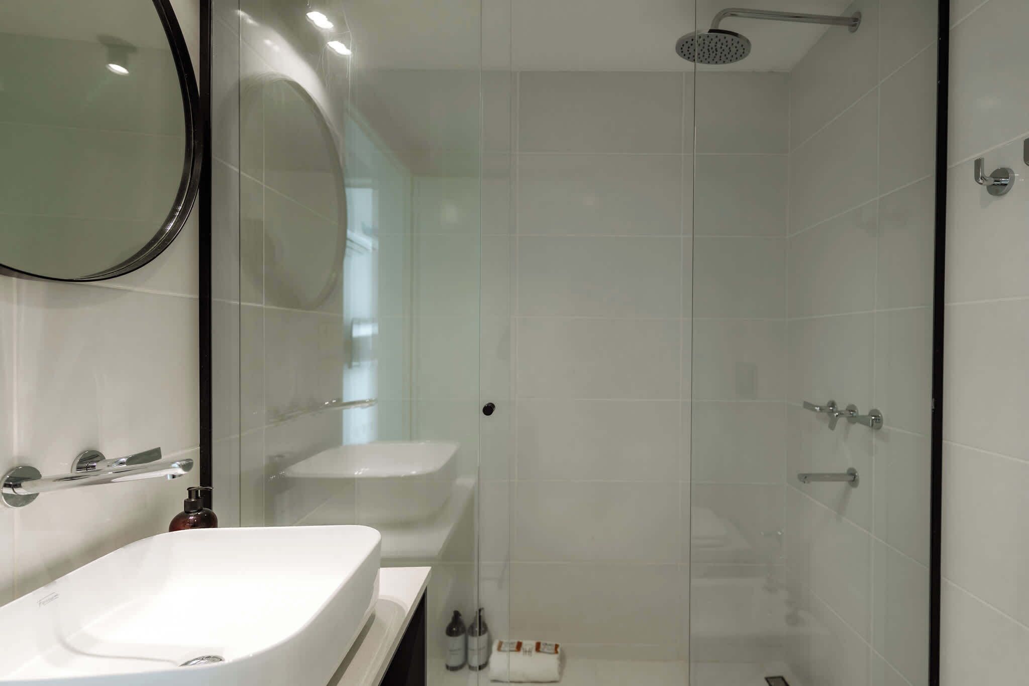Un baño moderno con un espejo grande, dos lavamanos, una ducha y zona de ducha con mampara de vidrio.