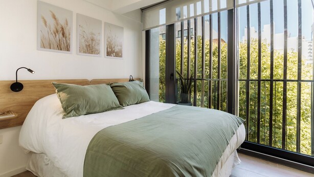 Quarto com uma cama grande, uma mesa de cabeceira, janela com vista para árvores e três quadros na parede.