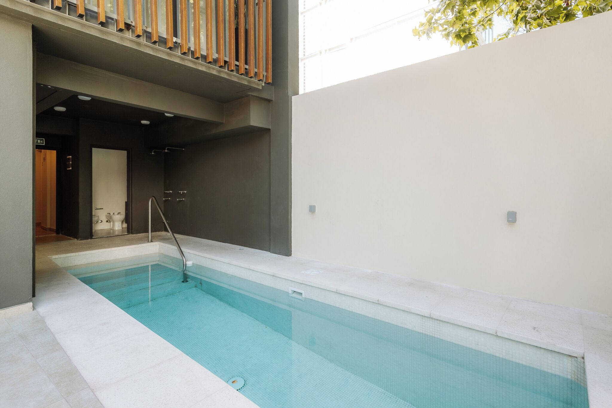 A swimming pool with a clear blue water, surrounded by a modern building with a balcony.